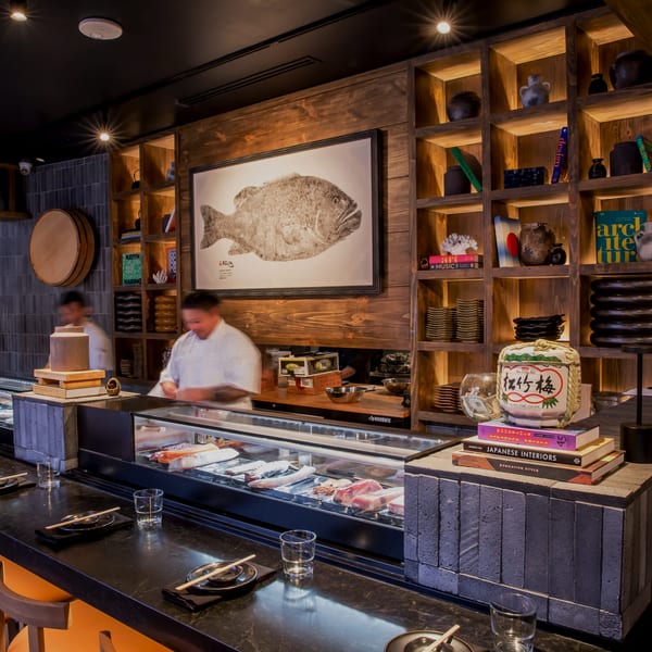 A sushi bar with chefs, fresh fish in a display case, and wooden shelves filled with decor.
