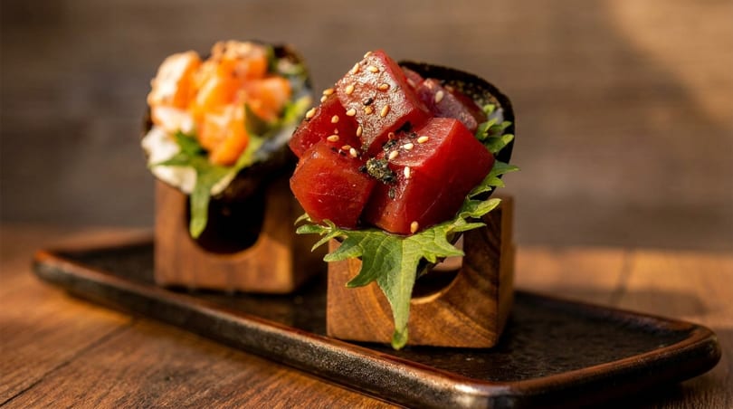 Two sushi hand rolls, one with tuna and the other with salmon, on a dark tray.