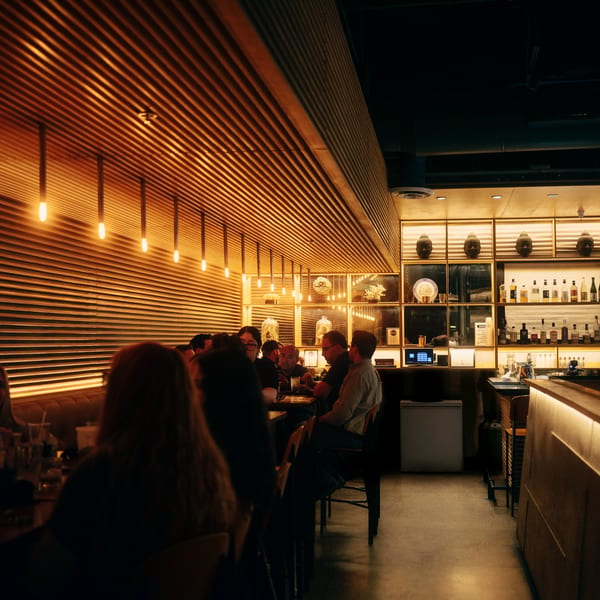 Diners seated at tables in a dimly lit restaurant with a bar and decorative Buddha heads.