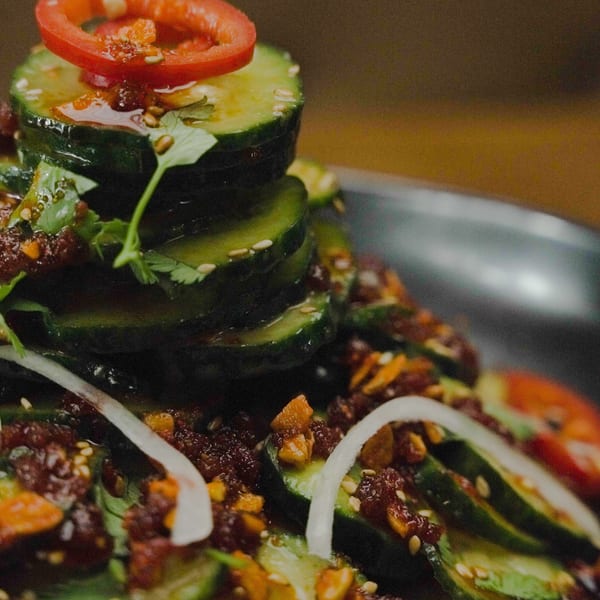 Cucumber salad with chili oil, sesame seeds, cilantro, and red pepper on a dark plate.