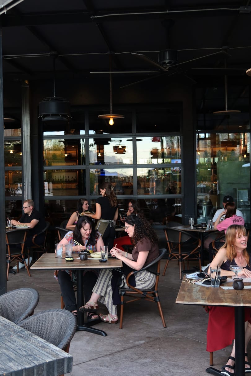Diners enjoy food and drinks on a bustling outdoor restaurant patio.
