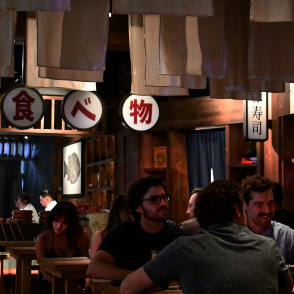 Diners seated at wooden tables in a dimly lit restaurant with Japanese-style decor and hanging banners.