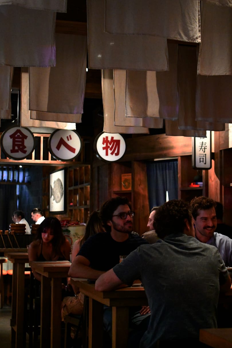 Restaurant interior with patrons dining under hanging fabric and Japanese character signs.