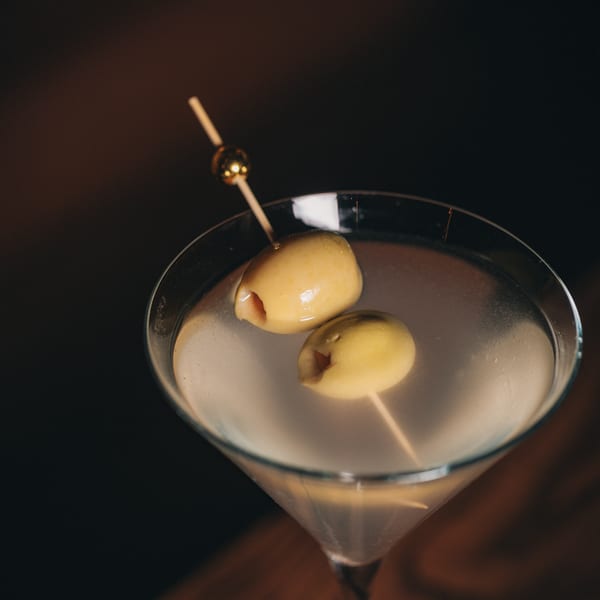 Martini glass with two green olives on a skewer against a dark background.