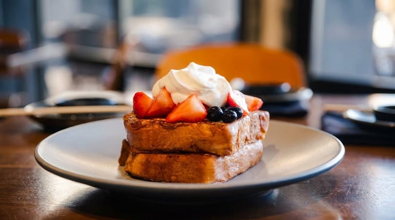 Two slices of French toast topped with whipped cream, strawberries, and blueberries on a white plate.