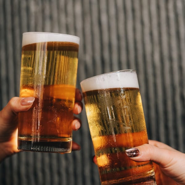 Two hands holding and clinking glasses of golden beer with foamy heads.