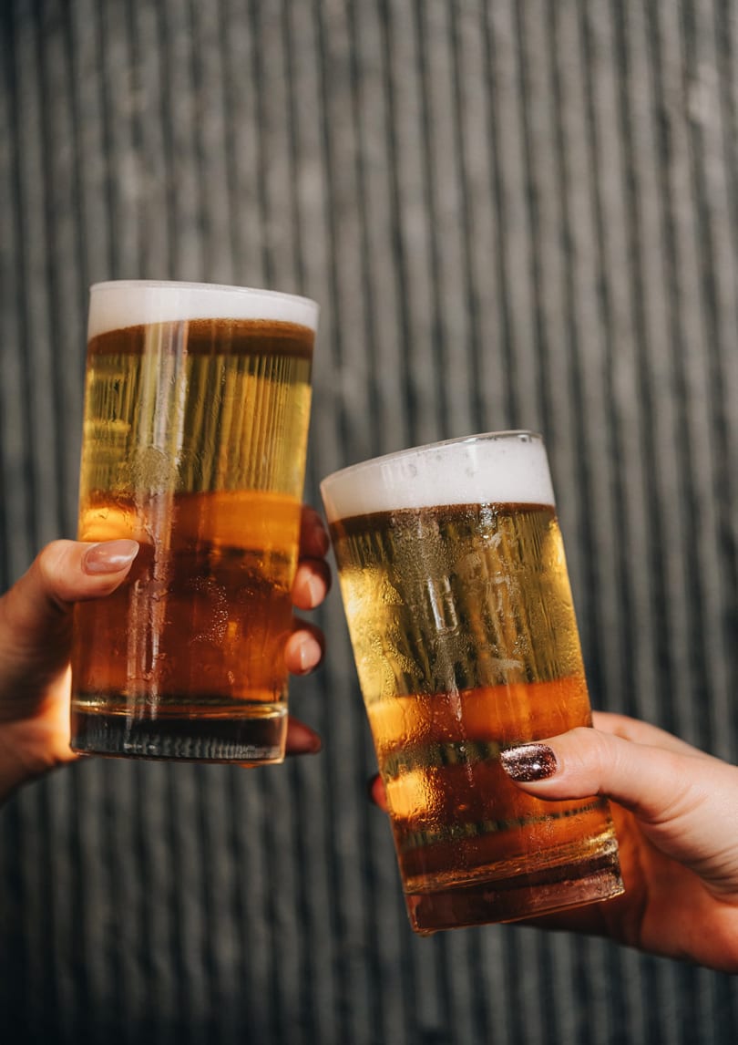 Two hands toast with frosty glasses of golden beer, showing foam and condensation.