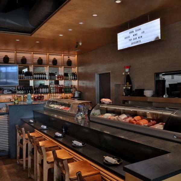 Interior of Obon Sushi restaurant with a sushi bar, wooden stools, and a menu board.