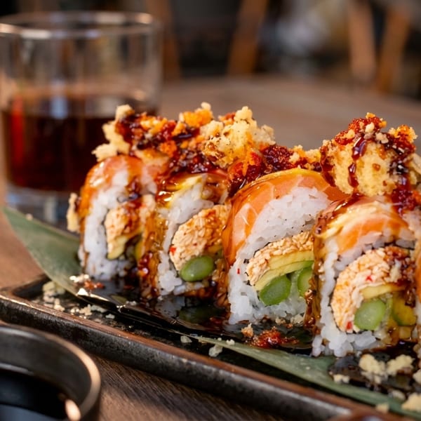 Sushi rolls with salmon, avocado, and sauce on a dark plate with a drink.