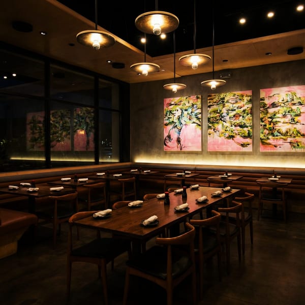 A dimly lit restaurant interior with wooden tables, chairs, and abstract art on the walls.