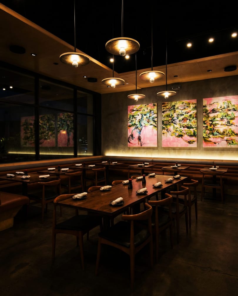 Dark, modern restaurant interior with wooden tables, booth seating, and abstract art on the wall.