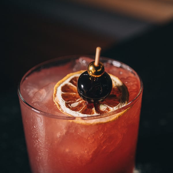 Close-up of a vibrant red cocktail with a dried orange and a cherry garnish.