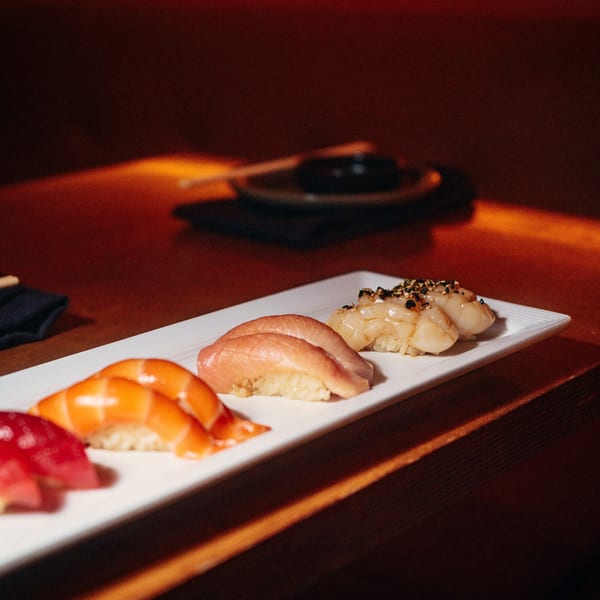 A white rectangular plate of various nigiri sushi on a dark wooden table.
