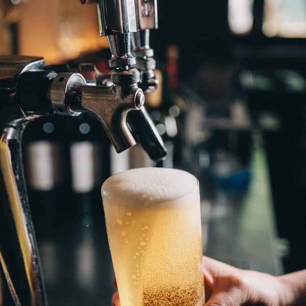 Hand pouring a golden beer from a tap into a glass, creating a foamy head.