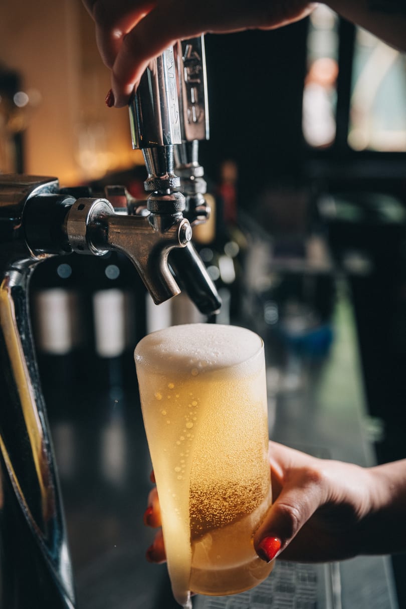 Hand pouring a golden beer from a tap into a glass, creating a foamy head.