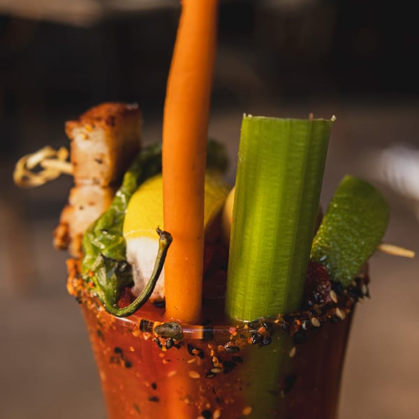 Close-up of a Bloody Mary cocktail garnished with bacon, lemon, pepper, carrot, celery, and lime.