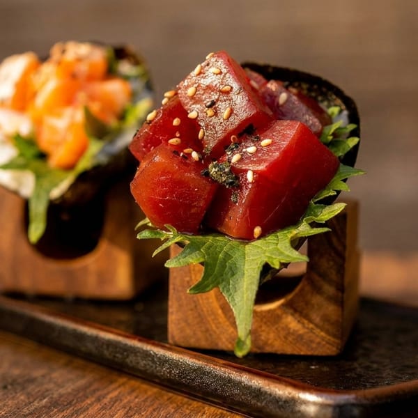 Two sushi hand rolls, one with tuna and the other with salmon, on a dark tray.