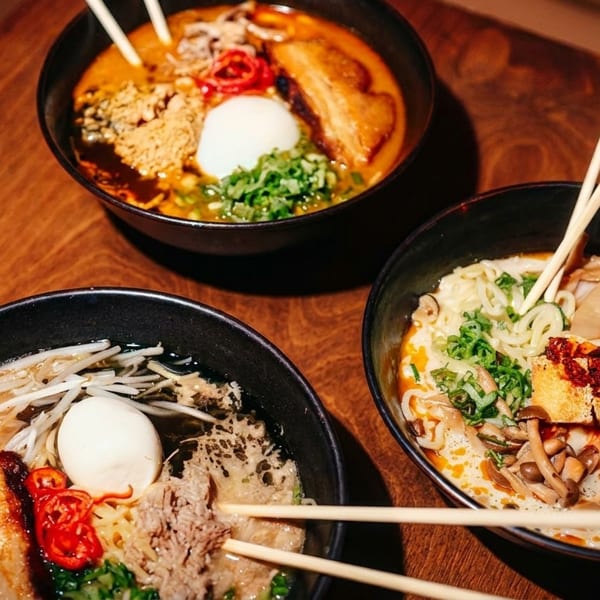 Three bowls of ramen with various toppings, including pork belly, egg, and vegetables, on a wooden table.